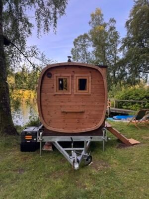 Frontansicht der mobilen Sauna TimberIN Nordic Square auf einem Anhänger an einem See