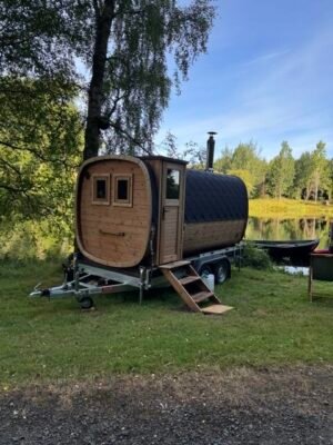Seitenansicht der mobilen Sauna TimberIN Nordic Square auf einem Anhänger mit Schornstein an einem See