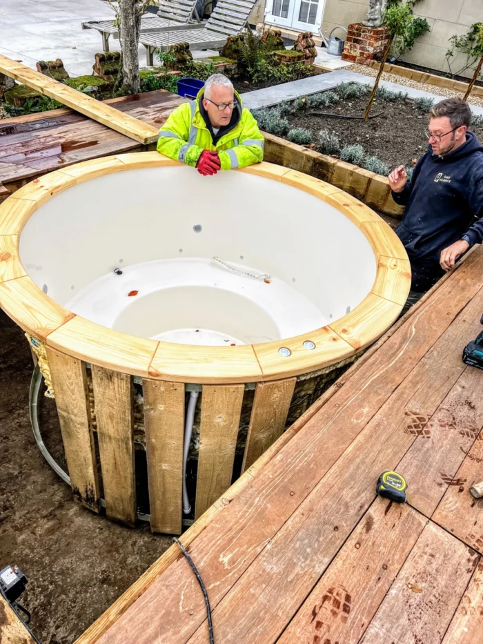 Zwei Personen beim Einbau einer hellen Badefass-Wanne in eine Holzterrasse