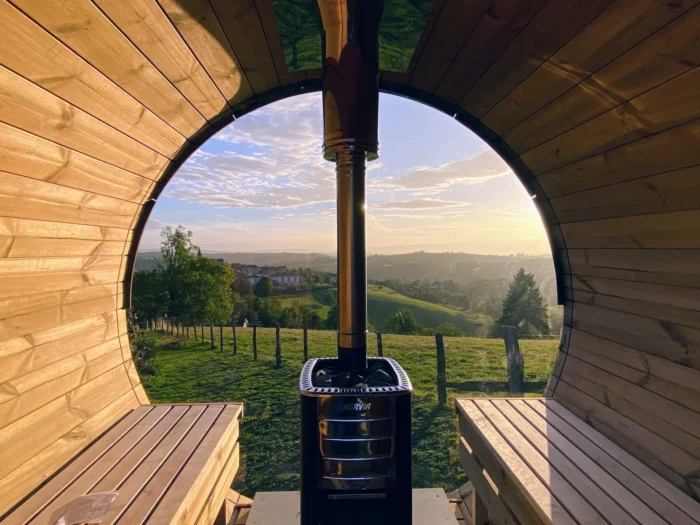 Holzofen vor einem großen runden Saunafenster mit Blick auf die Landschaft