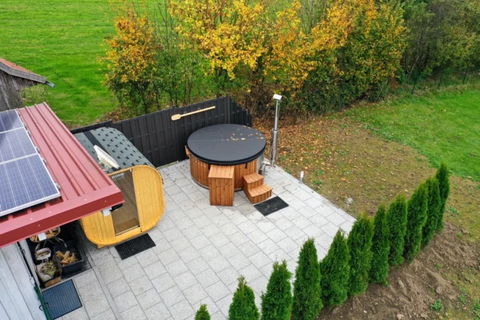 Blick von oben auf ein abgedecktes Badefass auf einer gepflasterten Gartenfläche