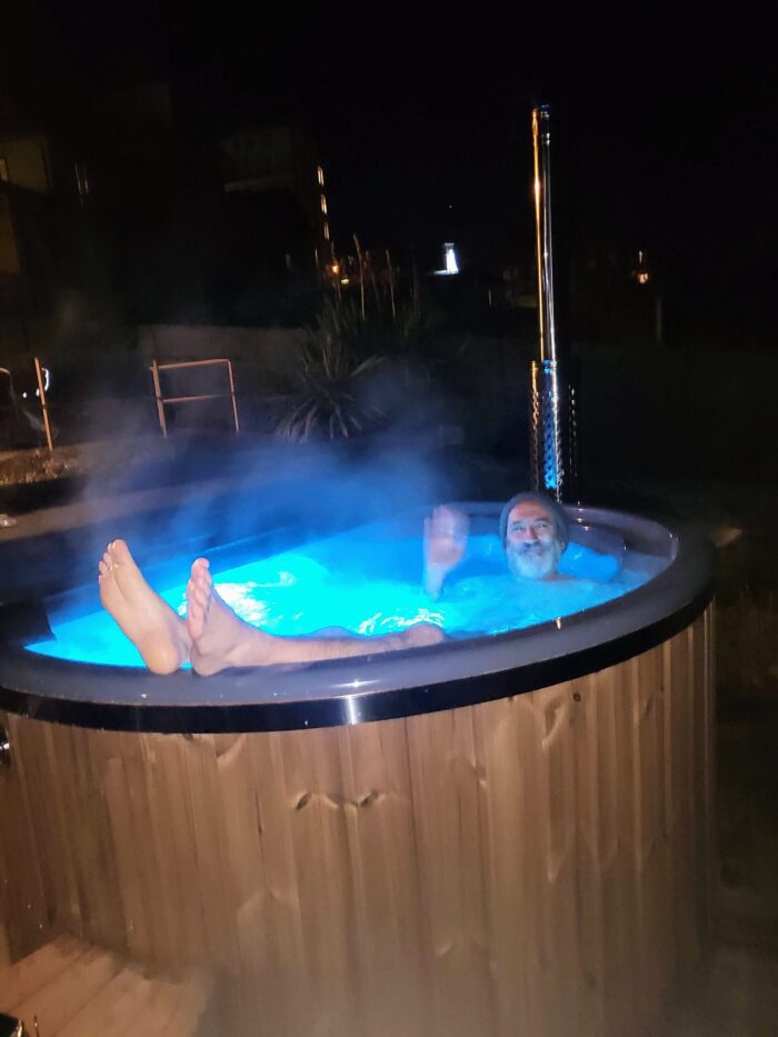 Whirlpool mit Holzofen 1 Badefass mit beleuchtetem Wasser und aufsteigendem Dampf am Abend