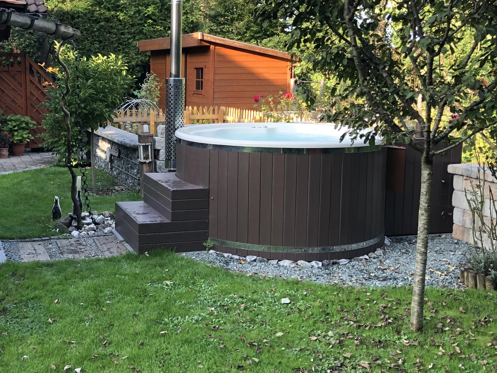 Badefass 1 Rundes Badefass mit heller Innenwanne, Holzverkleidung und Treppe in einem grünen Garten.