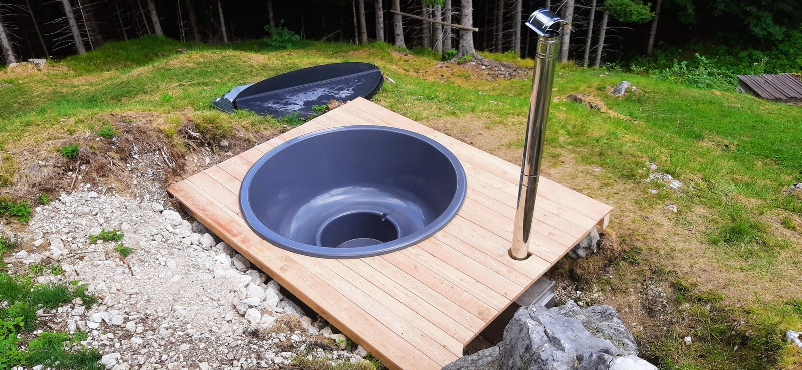 Einbau 1 Graue runde Badefasswanne mit Sitzbank, in ein Holzdeck eingelassen, mit Schornstein neben dem Becken